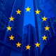 The flag of the European Union (a circle of yellow stars on a blue background) is superimposed on a trio of glass skyscrapers